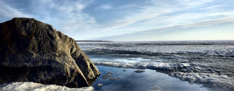 A large rock in the foreground with a frozen lake and blue sky