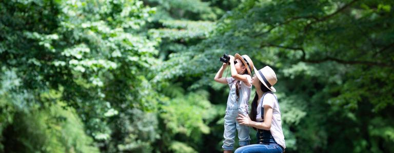 Daughter and mother looking through binoculars at a river bank