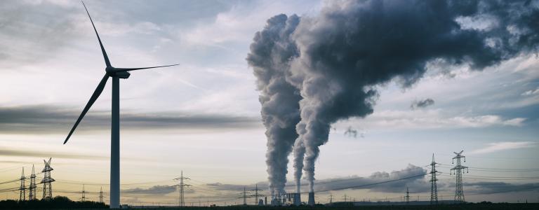 Single wind turbine with a coal burning power plant and pollution in the background.