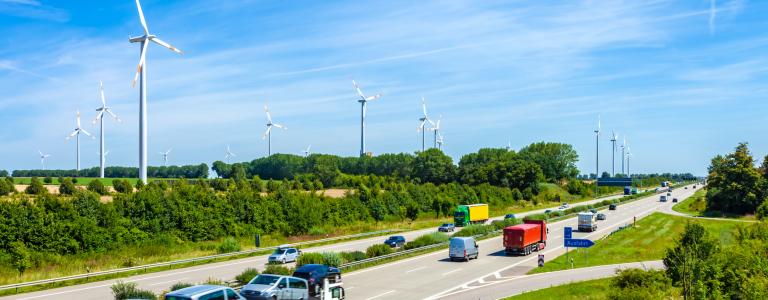 Vehicles drive along a highway next to a wind energy farm. 