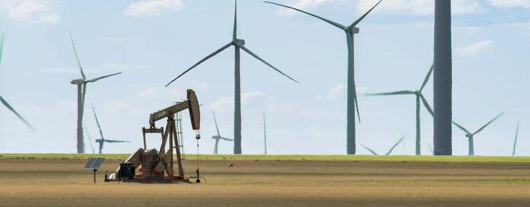 Single oil pump in a field surrounded by wind turbines.