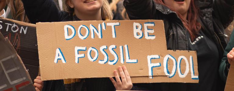 Youth hold protest signs, with one reading "Don't be a fossil fool".