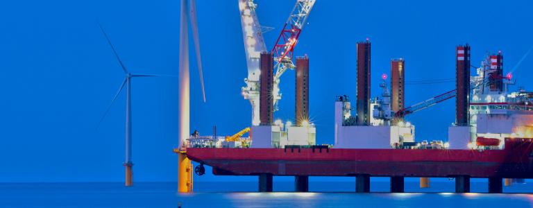 A wind turbine is constructed at sea, at dusk.