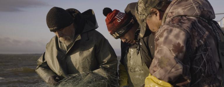 fishermen look down at a net and boat on a lake