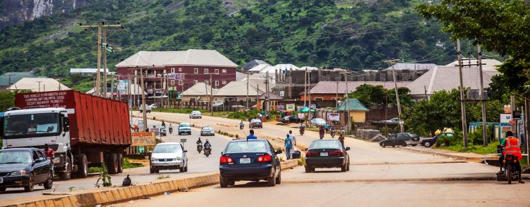 Cars driving on a road in Nigeria with a mountain backdrop on a cloudy day