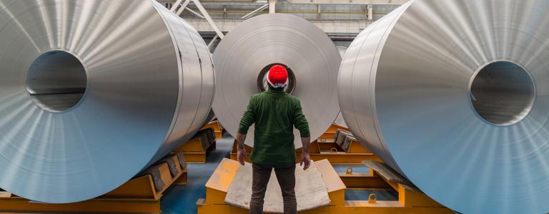 Worker standing in the factory infront of large aluminum rolls.