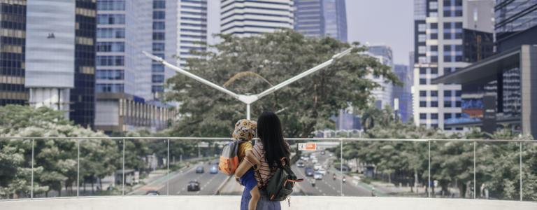 Mother and son carrying rucksack while standing in front of a city skyline.