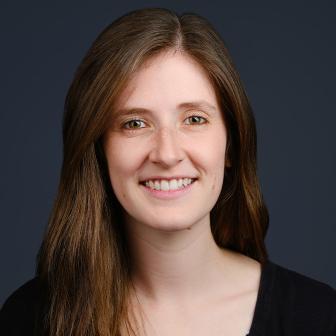 woman with dark brown hair smiling against a dark background