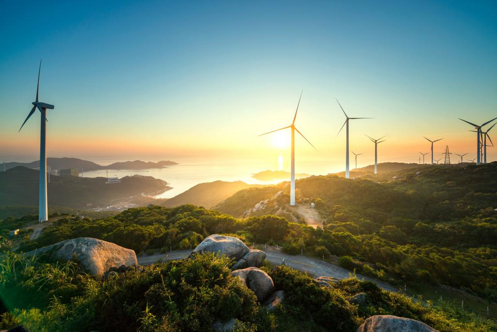 A row of wind turbines along rolling hills at sunset